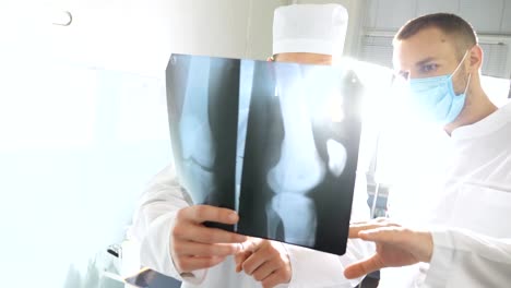 Two-caucasian-doctors-watching-to-mri-picture-and-discussing-about-it.-Male-medics-consult-with-each-other-while-looking-at-x-ray-image.-Medical-workers-in-hospital-examine-x-ray-prints.-Close-up-Front-view