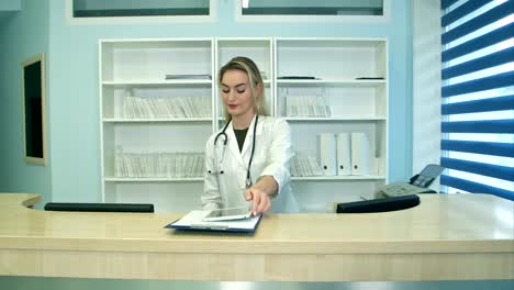 Busy-young-nurse-using-tablet-and-phone-at-reception-desk