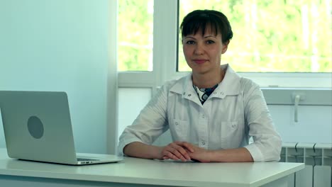 Female-doctor-working-at-office-desk-with-laptop-and-smiling-at-camera