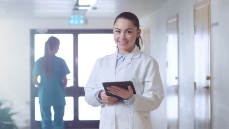 Schöne-junge-Frau-Doktor-steht-auf-dem-Krankenhaus-Flur,-Tablettcomputer-benutzt-und-lächelt-charmant.-Professionelle-Leute-bei-der-Arbeit.