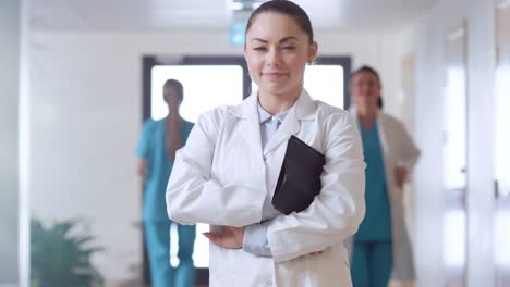 Hermosa-joven-doctora-paseos-por-el-pasillo-del-Hospital,-se-detiene,-cruza-los-brazos-y-encantadora-sonrisa.-Gente-profesional-en-el-trabajo.