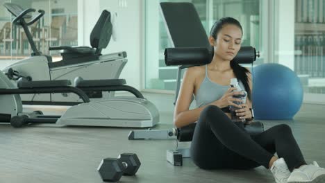 Asian-woman-in-gym-drink-water-after-exercise