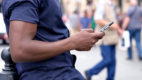 negro-de-manos-de-hombre-americano-mecanografiar-en-el-smartphone-en-la-ciudad