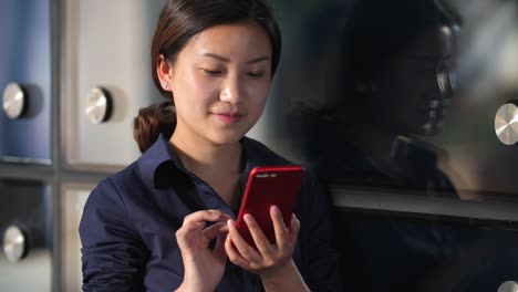 Young-Asian-Businesswoman-Looking-at-her-Mobile-Phone-by-the-Office-Window-Glass,-Slow-motion-4k