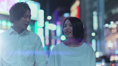 Young-Japanese-Boy-and-Girl-Couple-Walking-and-Talking.-In-the-Background-Blurred-Advertising-Billboards-and-City-Lights-at-Night.