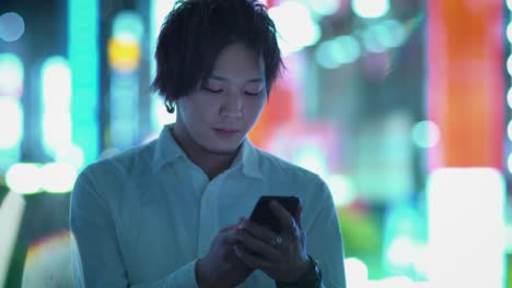 Portrait-of-the-Handsome-Alternative-Japanese-Boy-Using-Smartphone.-In-the-Background-Big-City-Advertising-Billboards-Lights-Glow-in-the-Night.