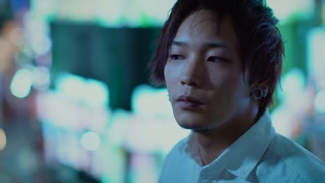 Porträt-der-hübsche-junge-japanische-Mann,-Blick-auf-die-Lichter-der-Großstadt.-Im-Hintergrund-Plakate-Großstadt-Werbung-Lichter-leuchten-in-der-Nacht.