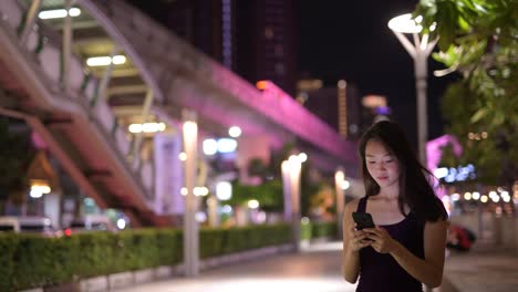 Schöne-asiatische-Frau-draußen-in-der-Nacht-mit-Handy