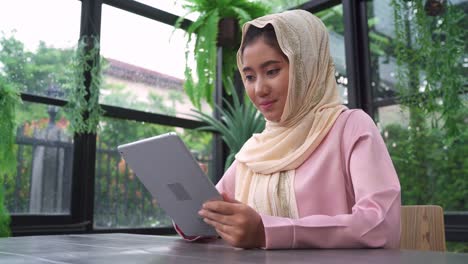 Hermosa-joven-sonriente-a-mujer-musulmana-asiática-utilizando-tablet-sentado-en-la-sala-de-estar-en-casa.-Disfrutando-en-casa.