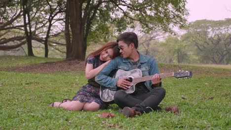 Young-asian-couple-spending-time-together-in-the-park,-playing-guitar,-talking,-enjoying.