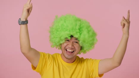 Young-crazy-man-with-colored-afro-wig-expressing-happiness-on-pink-background.