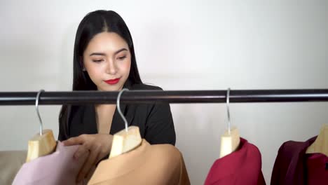 Junge-asiatische-Frau-durchsuchen-und-wählen-Sie-Kleidung-von-bunten-Anzug