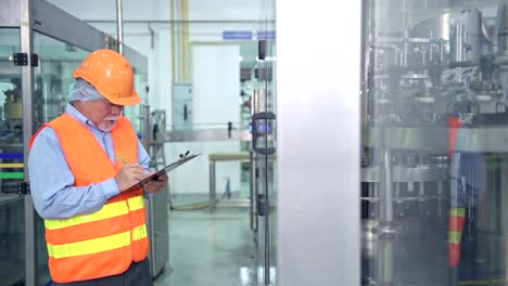 Quality-inspection-in-factory.-Senior-chinese-quality-assurance-team-inspecting-a-liquid-filling-bottle-machine-in-factory-using-TQM,-TPM-methodology.-Excellence-manufacturing-concept.