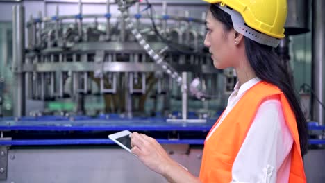 Mujer-ingeniero-industrial-en-el-trabajo-en-la-fábrica.-Hermosa-joven-ingeniero-chino-trabajando-en-fábrica-grande.-Con-casco-y-chaqueta.-Máquina-automática-de-alta-tecnología-en-segundo-plano.