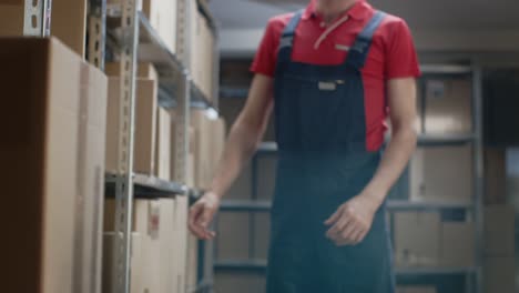 Warehouse-Worker-Walks-into-Storeroom-with-a-Cardboard-Box-and-Puts-it-on-a-Shelf.