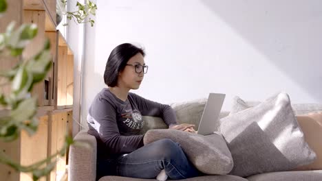 Schöne-Asiaten-junge-Frau-arbeiten-mit-Computer-Laptop-sitzend-auf-Sofa-zu-Hause.-Arbeit-zu-Hause-Konzept