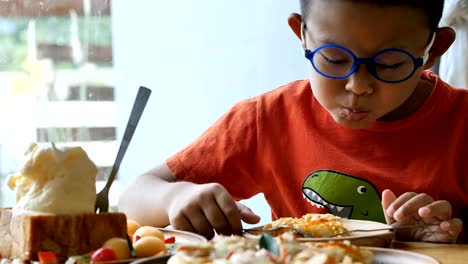 Cute-asian-children-holding-in-fork-and-knife-cuts-the-eating-pizza-in-the-restaurant