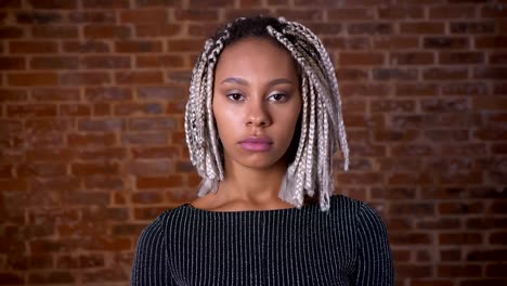 Young-African-serious-girl-with-dreadlocks-girl-looking-at-camera,-closing-eyes,-Brick-wall-in-the-background.