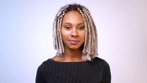 Chica-africana-joven-con-rastas-sonriendo-y-mirando-a-cámara,-blanco-de-la-pared-el-fondo.