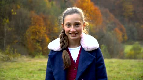 Una-hermosa-joven-está-de-pie-en-el-bosque-de-otoño,-mirando-a-la-cámara-y-sonriendo.-Ella-es-feliz.