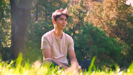 Dreaming-asian-boy-is-hanging-out-alone-in-park,-sitting-on-the-grass-in-sunlights,-fresh-spring-atmosphere