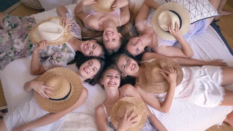 joyful-girlfriends-in-pajamas-lie-on-bed-with-straw-hats-on-faces-and-then-take-off-them-and-smile-into-camera-during-hen-party