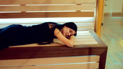 Beautiful-girl-lies-on-a-wooden-bench-in-the-sauna-behind-a-glass-door.-Girl-lies-with-her-eyes-closed.-Span-camera.-Portrait-view