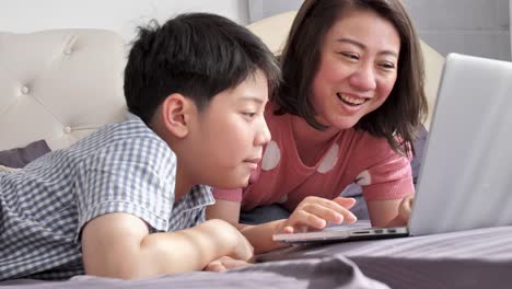 Glückliche-Familie-Mutter-und-Sohn-gerade-auf-Laptop-Computer-mit-Lächeln-Gesicht,-Slow-Motion-4K-asiatischen-Familie-Rest-auf-Bett-mit-Laptop-computer