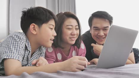 Glückliche-Familie-Vater-Mutter-und-Sohn-auf-Laptop-Computer-beobachten-und-Spaß,-Slow-Motion-4K-asiatischen-Familie-Rest-auf-Bett-mit-Laptop-computer