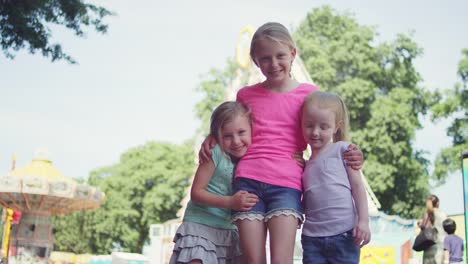 Three-little-girls-at-a-fair-give-a-group-hug-and-smile-at-the-camera