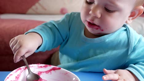 Un-atractivo-chico-de-2-años-come-una-ensalada-de-remolacha-roja.-La-cara-está-manchada-con-gachas-de-avena.-Se-sienta-en-la-mesa