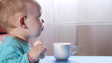 An-attractive-boy-2-years-old-eats-a-banana.-Sits-at-the-table-at-home.-Carefully-watching-cartoons-on-TV