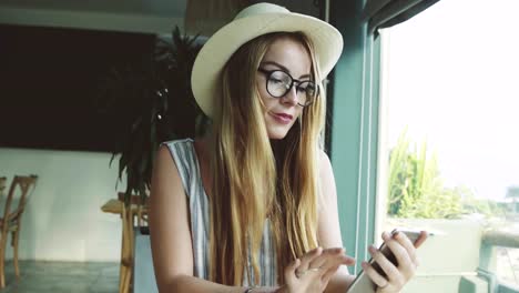 Frau,-die-durch-Bilder-auf-Smartphone-im-Café.-Schöne-junge-Mädchen,-trinken-Kaffee-und-lächelt.