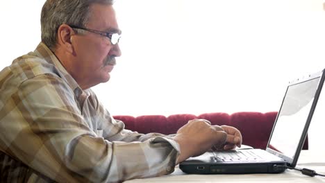 Senior-man-in-glasses-works-for-a-laptop.-He-looks-seriously-at-the-monitor