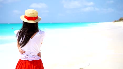 Back-view-of-beautiful-woman-in-hat-on-summer-holidays-on-white-beach.