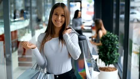 Mujer-joven-con-bolsas-sonriendo-y-posando.-Luces-de-tiendas-en-fondo