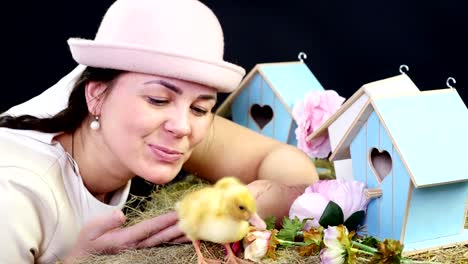 Portrait,-a-pretty-young-woman-with-two-pigtails-and-in-a-funny-pink-hat-playing-with-small-yellow-ducklings.-Studio-video-with-thematic-decor