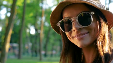 A-portrait-of-a-beautiful-young-woman-wearing-hat-and-sun-glasses-smiling-in-park