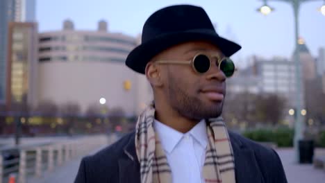 Hombre-joven-con-origen-étnico-afroamericano-con-Look-clásico-antiguo.-Divertirse-en-la-gran-ciudad-con-gafas-de-sol,-sombrero-y-bufanda.