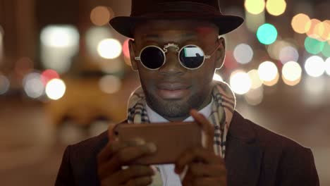 Hombre-joven-con-origen-étnico-afroamericano-con-Look-clásico-antiguo.-Divertirse-en-la-gran-ciudad-con-gafas-de-sol,-sombrero-y-bufanda.