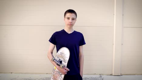 Image-of-handsome-teenager-standing-in-the-street-and-holding-skateboard-in-his-hands.-Boy-spending-free-time-in-skateboarding-park-demonstrating-healthy-lifestyle-and-looking-at-the-camera