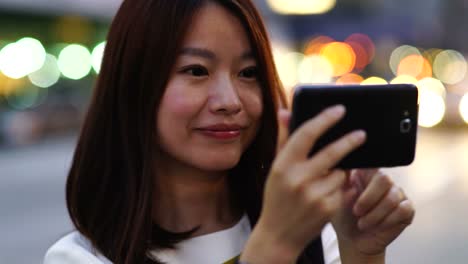 Attraktive-asiatische-Frau-mit-Telefon-in-der-Stadt.-Dunkle-Augen-und-dunkle-Haare.-Überfüllt-und-urbanen-Hintergrund.