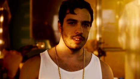 Smoking-Brutal-Gang-Member-with-Gold-Chain-Looks-into-Camera-with-Defiance.-Underground-Drug-Laboratory-is-in-Background.