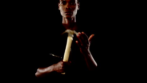 Androgynous-man-posing-with-hammer-against-black-background