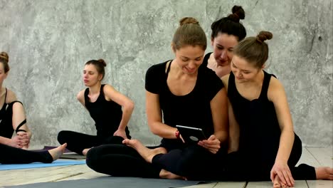 Portrait-of-smiling-fit-women-using-digital-tablet-while-sitting-at-yoga-mat-after-fitness-workout