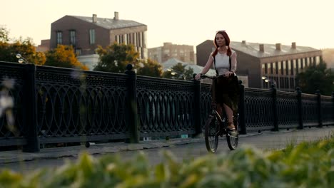 Red-haired-woman-riding-bicycle-in-city-on-background-facade-building