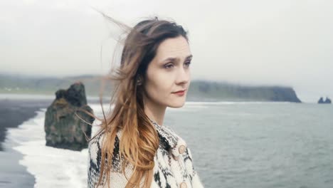 Porträt-des-jungen-lächelnde-Frau-stand-am-schwarzen-Strand,-Troll-Zehen-auf-dem-Hintergrund-in-Island,-Blick-in-die-Kamera