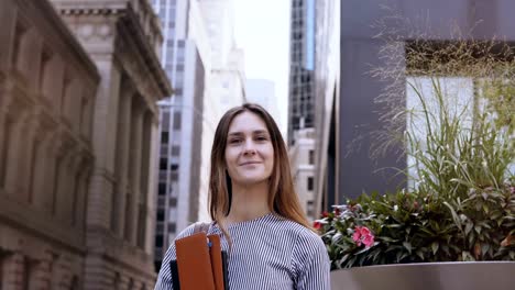 Portrait-of-young-beautiful-successful-businesswoman-near-office-building-in-New-York,-America.-Female-holds-documents