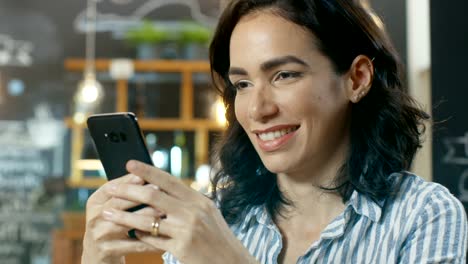 Porträtaufnahme-von-einer-schönen-jungen-Frau-lächelnd-und-Mobiltelefon-zu-benutzen.-Im-Hintergrund-stilvollen-Cafe.