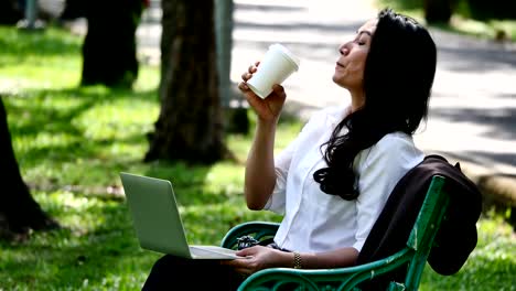 Asian-business-woman-using-laptop-and-drinking-coffee-in-the-park.